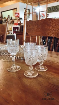 three glass goblets sitting on top of a wooden table in front of chairs