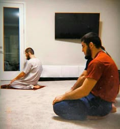 two men sitting on the floor in front of a flat screen tv watching another man