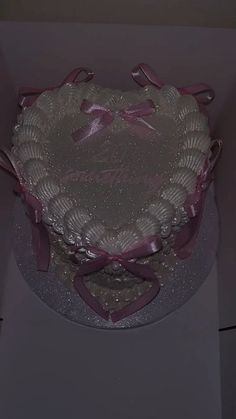 a heart shaped cake sitting on top of a white table with pink ribbon around it