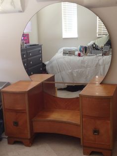 a bedroom with a dresser and mirror in the corner, next to a bed that has a white sheet on it