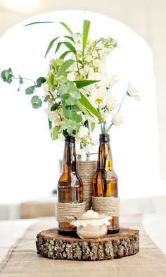 two beer bottles with flowers in them sitting on a piece of burlocked wood