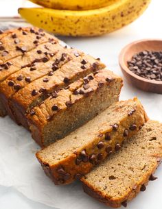 sliced loaf of banana bread with chocolate chips on top and two bananas in the background