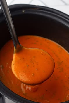 a ladle full of tomato soup being held by a wooden spoon in a black pot