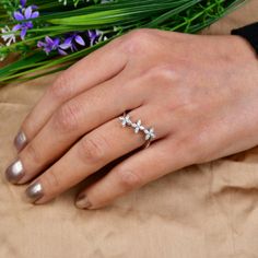 a woman's hand with a ring on it and flowers in the back ground