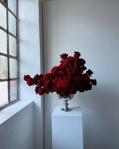 a vase filled with red roses sitting on top of a white pedestal next to a window