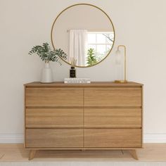 a wooden dresser with a mirror and plants on it in front of a white wall