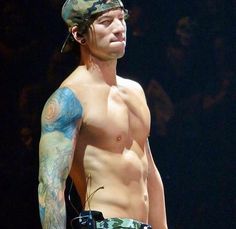 a shirtless man with tattoos on his arm and chest standing in front of a black background