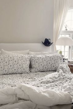 a bed with white sheets and pillows in a room next to a lamp on a table