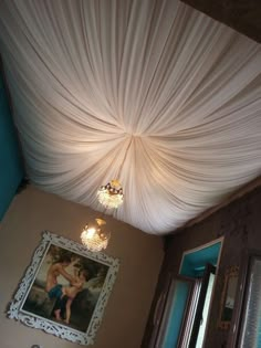 the ceiling is covered with white draping and chandelier hanging from it