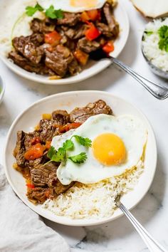 two plates filled with rice, meat and an egg on top of each other next to bowls of vegetables