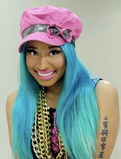 a woman with blue hair wearing a pink hat and chain around her neck is smiling at the camera