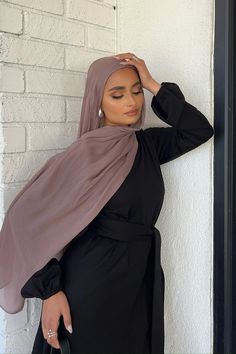 a woman wearing a hijab leaning against a wall with her hand on her head