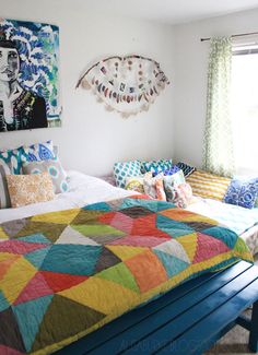 a bed with colorful quilts and pillows in a white room next to a window