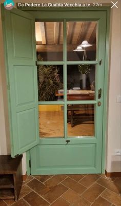 an open green door in front of a table and chair with a lamp on it