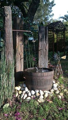 an old barrel is sitting in the middle of some rocks and grass, next to two wooden poles