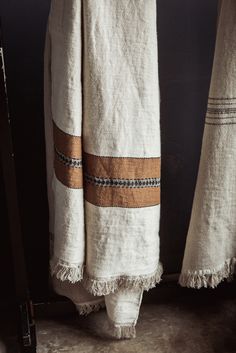 two white towels hanging on a rack in front of a black wall, with one folded up and the other closed