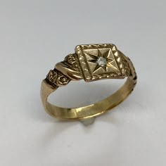 a gold ring with a diamond in the center on a white surface, it looks like an old fashioned ring