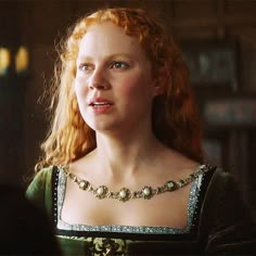 a woman with red hair wearing a green dress and gold necklace in a dark room