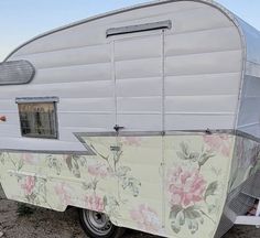 an old camper is parked in the dirt with flowers on it's side