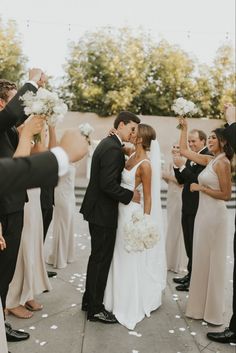 a bride and groom kissing in front of their wedding party with confetti on the ground