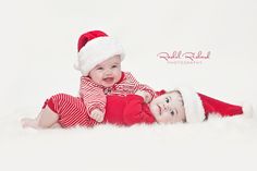 two babies are laying on the floor wearing santa hats and red striped onesuits