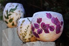 three vases with flowers painted on them are lined up against a stone fence post