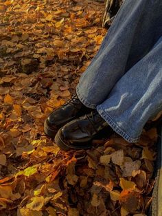 a person is sitting on a bench with their feet propped up against the ground covered in leaves