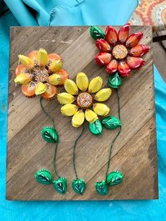 three flowers are sitting on top of a wooden board with green leaves and beads in the middle