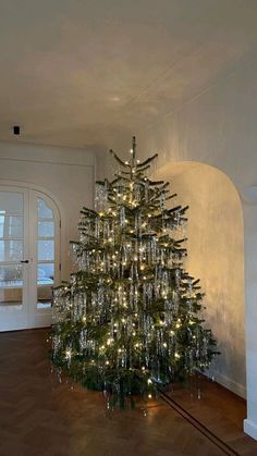 a christmas tree with lights is in the middle of an empty room, surrounded by wood flooring