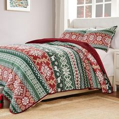 a bed with a red and green blanket on top of it next to a window