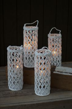 four white candle holders sitting on top of a wooden table next to each other with lit candles in them