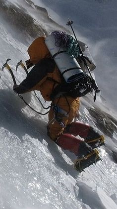 a man walking up the side of a snow covered mountain with skis on his back