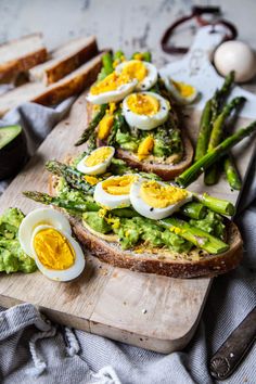 an egg and avocado toast with asparagus on a wooden cutting board