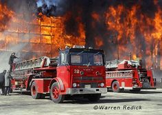 two firetrucks are parked in front of a building with flames behind them