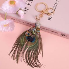 a keychain with a peacock feather on it sitting next to flowers and a pair of scissors