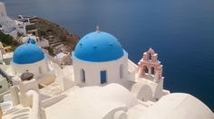 two white and blue domes on top of a building next to the ocean with water in the background