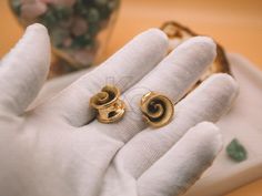 a pair of gold earrings sitting on top of a white glove