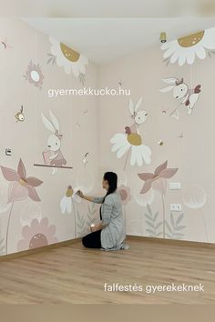 a woman sitting on the floor in front of a wall with flowers and birds painted on it