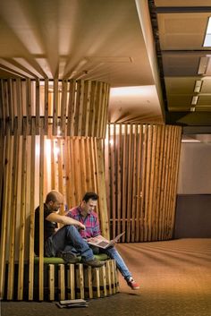 two men are sitting on a bench in an office building with wooden slats covering the walls