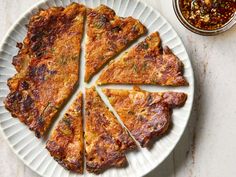 a white plate topped with slices of pizza next to a bowl of chili and seasoning