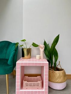 a pink brick side table next to a green chair and potted plant on the floor