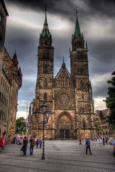 people are walking around in front of an old building with tall towers and spires