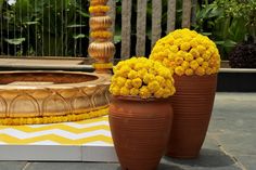 two large vases filled with yellow flowers sitting on top of a cement floor next to a fountain