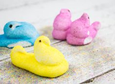 three small toy birds sitting on top of a wooden table with sprinkles