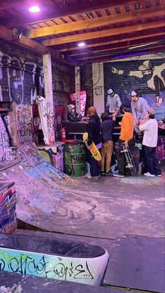 a group of people standing around a skateboard park with graffiti on the walls and ceiling