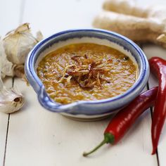 a bowl filled with soup next to two red chili peppers and garlic on a table