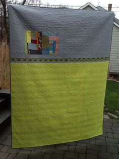 a green and gray quilt hanging from a clothes line on a clothes line in front of a house