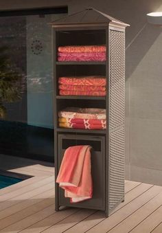 an outdoor storage unit with towels and blankets on it next to a swimming pool in the background