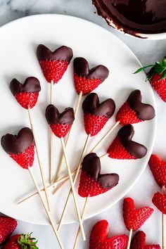 chocolate covered strawberries are arranged on a white plate next to some strawberries with hearts