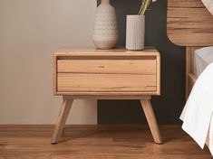 a wooden nightstand with two vases on top of it next to a white bed